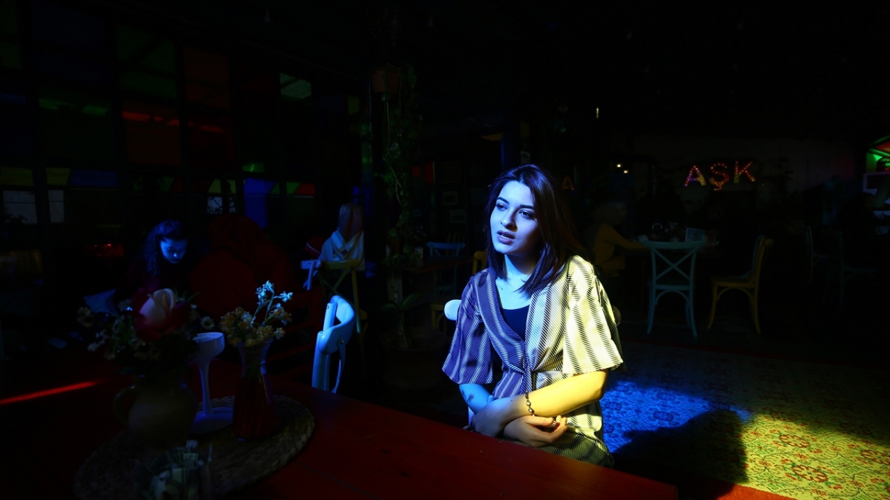 Kafede gündüz vakti oturanlar renkli pencerelerden yansıyan güneş ışığıyla aydınlanıyor.