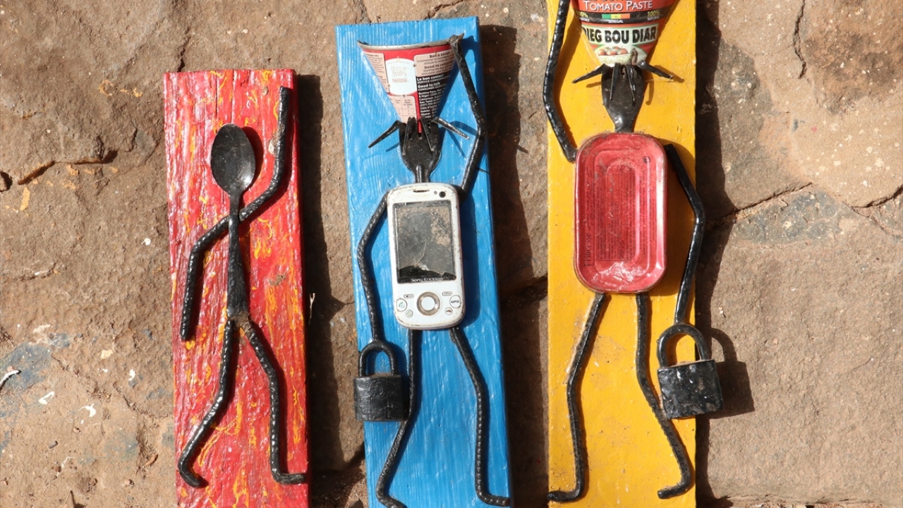 Adalıların "Yaşlı Mbodji" ismini verdiği sanatçı, cep telefonu, saat, hesap makinesi, fotoğraf makinesi, kaşık, çatal, konserve kutusu, gazoz kapağı gibi çeşitli atıkları kullanarak yaptığı tabloların her birinin ayrı anlamı olduğunu dile getirdi. 