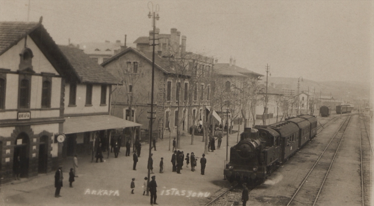 Fotoğrafta, eski Ankara İstasyon Binası ve İstasyon önünde insanlar ve kara tren görülüyor.