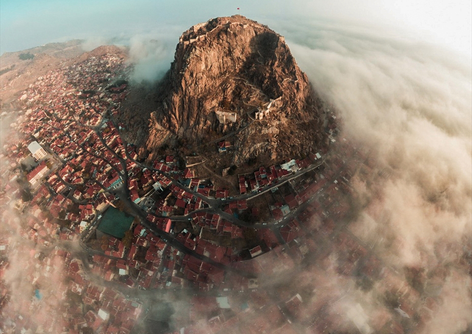 Fotoğrafta bir tarafı sisler içinde kalan kale ve şehir görünürken diğer tarafta güneşin aydınlattığı şehir yer alıyor.